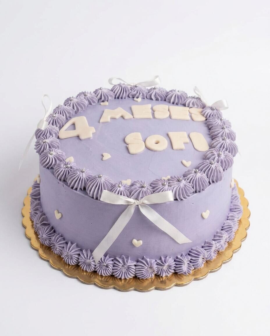 Pastel redondo en buttercream lila con letras color crema '4 MESES SOFI', borde de rosetones piped en lila con perlas plateadas, dos moñitos de satén crema arriba y un moño grande de satén crema al frente, sobre base dorada festoneada